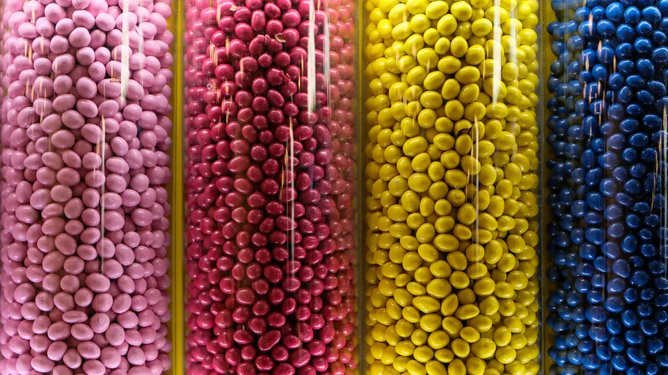 Vier hohe Glasröhren, gefüllt mit rosa, roten, gelben und blauen Zuckerkügelchen
